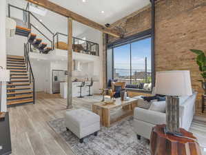 Living room featuring brick wall, beamed ceiling, a towering ceiling, and light hardwood / wood-style floors