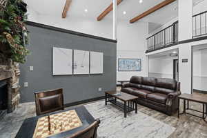 Living room with a stone fireplace, wood-type flooring, high vaulted ceiling, and beam ceiling