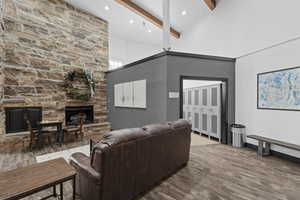 Living room with beamed ceiling, light hardwood / wood-style flooring, a stone fireplace, and high vaulted ceiling