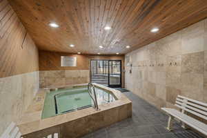 Bathroom featuring wood ceiling, tile walls, tile patterned floors, a tub, and wood walls