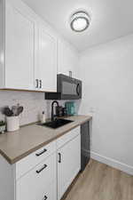 Kitchen featuring sink, light wood-type flooring, white cabinets, and backsplash