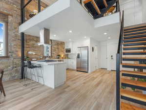 Kitchen with light hardwood / wood-style flooring, stainless steel appliances, island range hood, white cabinets, and kitchen peninsula