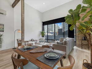 Dining room with a wall unit AC, light hardwood / wood-style flooring, and a towering ceiling