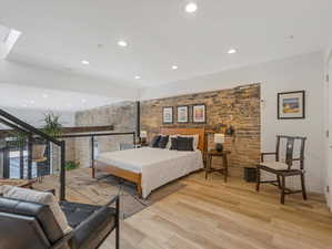 Bedroom featuring a skylight, multiple windows, brick wall, and light wood-type flooring