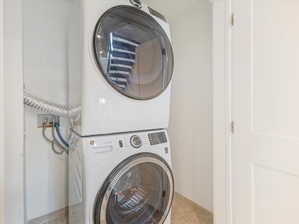 Clothes washing area featuring light tile patterned flooring and stacked washer and dryer