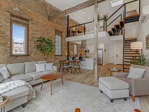 Living room with brick wall, light hardwood / wood-style flooring, and a high ceiling