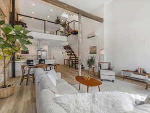 Living room with light hardwood / wood-style floors, a wall unit AC, and a high ceiling