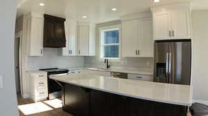 Kitchen featuring appliances with stainless steel finishes, sink, premium range hood, light wood-type flooring, and a center island