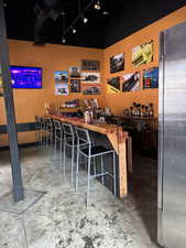 Bar featuring butcher block countertops, track lighting, stainless steel refrigerator, and concrete floors