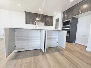 Kitchen with dark brown cabinets, oven, stainless steel microwave, light hardwood / wood-style flooring, and kitchen peninsula