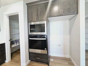 Kitchen with light wood-type flooring, dark brown cabinets, stainless steel oven, and black microwave