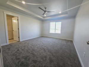 Carpeted empty room featuring ceiling fan and a tray ceiling