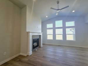 Unfurnished living room with lofted ceiling, wood-type flooring, a tiled fireplace, and ceiling fan