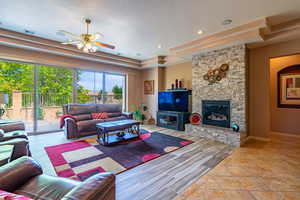 Living room featuring light tile patterned flooring, a stone fireplace, ceiling fan, and a wealth of natural light from the sliding glass doors