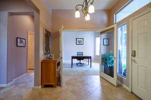 Tiled entryway with an inviting chandelier.  Looking into den/office with french doors