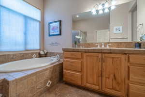 Bathroom featuring a wealth of natural light, vanity, tile patterned flooring, and tiled bath