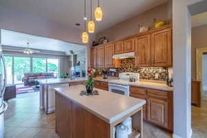 Kitchen with ceiling fan, tasteful backsplash, white appliances, a center island, and light tile patterned floors