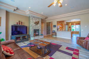 Living room featuring a stone fireplace, a raised ceiling, light tile patterned floors, and ceiling fan