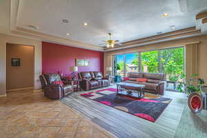 Living room with a textured ceiling, ceiling fan, and a tray ceiling