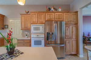 Kitchen featuring light tile patterned flooring, decorative backsplash, and white appliances including double ovens