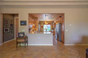 Kitchen featuring canned & pendant lighting, light tile patterned floors, kitchen peninsula, and stainless steel fridge