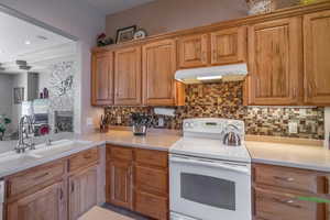 Kitchen with white electric range, tasteful backsplash, sink, reverse osmosis water system and kitchen peninsula