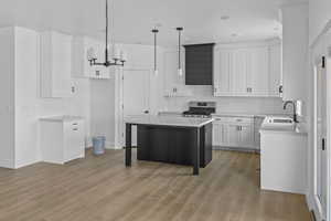 Kitchen with white cabinetry, light wood-type flooring, a center island, gas range, and sink