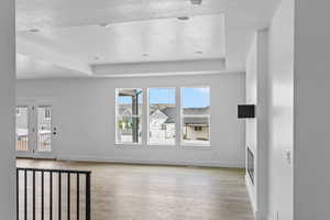 Unfurnished living room featuring a raised ceiling, light wood-type flooring, and a textured ceiling