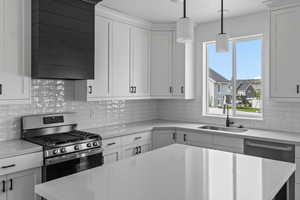 Kitchen featuring white cabinetry, tasteful backsplash, stainless steel appliances, decorative light fixtures, and sink