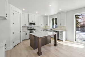 Kitchen with appliances with stainless steel finishes, white cabinets, sink, light hardwood / wood-style floors, and a kitchen breakfast bar