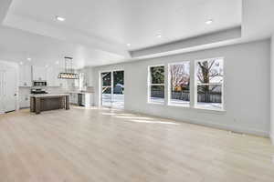 Unfurnished living room with sink, a tray ceiling, and light hardwood / wood-style flooring