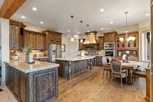 Kitchen with appliances with stainless steel finishes, tasteful backsplash, light stone counters, custom exhaust hood, and a large island with sink