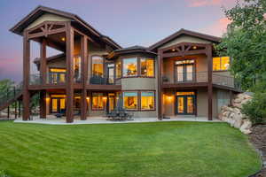 Back house at dusk with a balcony, a patio area, and a yard