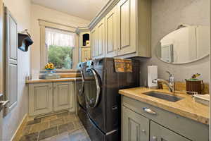 Laundry room featuring washer and clothes dryer, sink, dark tile patterned flooring, and cabinets