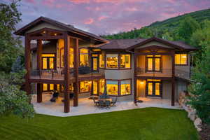 Back house at dusk featuring a patio, a balcony, a lawn, and a mountain view