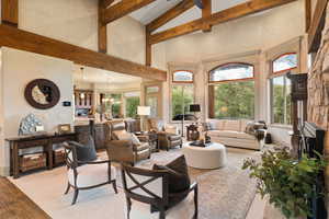 Living room featuring an inviting chandelier, beam ceiling, light hardwood / wood-style floors, and a towering ceiling