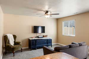 Living room with a textured ceiling, carpet floors, and ceiling fan