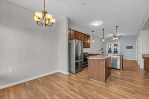 Kitchen with stainless steel appliances, pendant lighting, a kitchen island, hardwood flooring