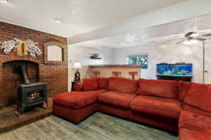 Living room with ceiling fan, a wood stove, hardwood / wood-style floors, and a textured ceiling