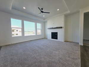 Unfurnished living room with carpet, a raised ceiling, a tile fireplace, and ceiling fan