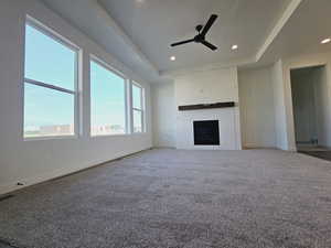 Unfurnished living room with ceiling fan, a tray ceiling, a brick fireplace, and carpet flooring