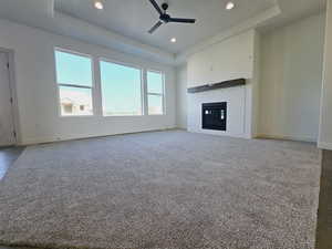 Unfurnished living room with ceiling fan, a tiled fireplace, a tray ceiling, and carpet flooring