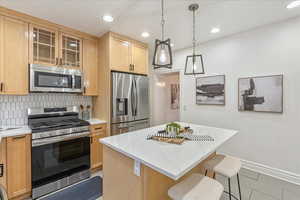 Kitchen featuring tasteful backsplash, light brown cabinets, a kitchen island, appliances with stainless steel finishes, and light tile patterned floors