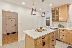 Kitchen featuring stainless steel dishwasher, light brown cabinetry, tasteful backsplash, a center island, and light tile patterned floors