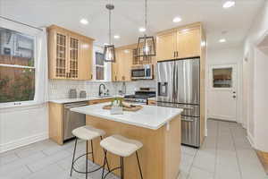 Kitchen featuring light brown cabinetry, a center island, appliances with stainless steel finishes, light tile patterned floors, and backsplash