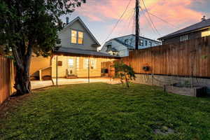 Back house at dusk featuring a patio and a yard