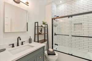 Full bathroom with toilet, enclosed tub / shower combo, and vanity