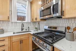 Kitchen with light brown cabinets, tasteful backsplash, stainless steel appliances, light stone countertops, and sink