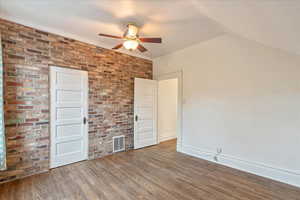 Third bedroom features wood-style floors, a vaulted ceiling, brick wall, and a ceiling fan