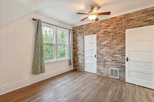 Third bedroom with exposed brick wall, ceiling fan, and hardwood / wood-style floors